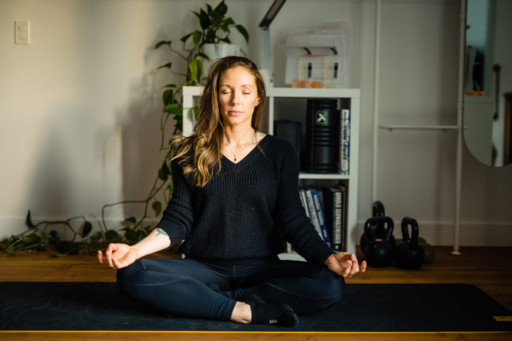 commercial photography of a long-haired woman sitting cross legged and meditating in a sparsely furnished room