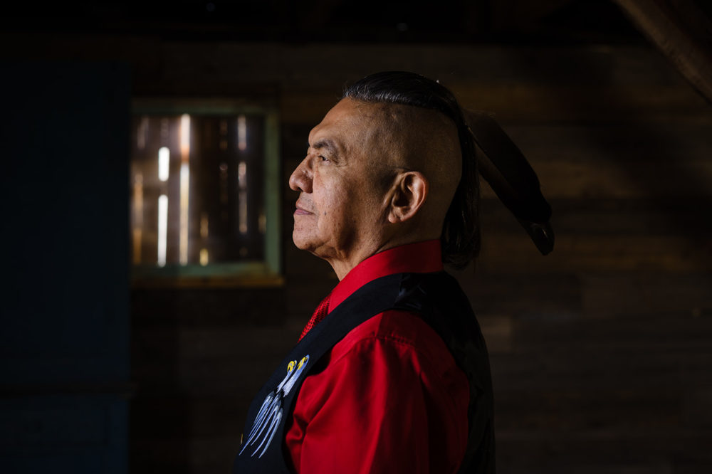 native man wearing red shirt and overalls looks toward a window slightly smiling in this image by sunshine coast commercial photographer sherry nelsen