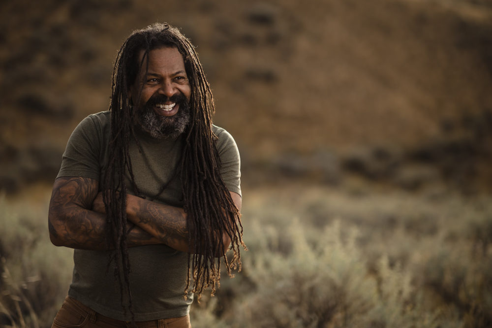 middle aged bearded black man with long braids and many tattoos smiles while getting headshots on the sunshine coast with sherry nelsen